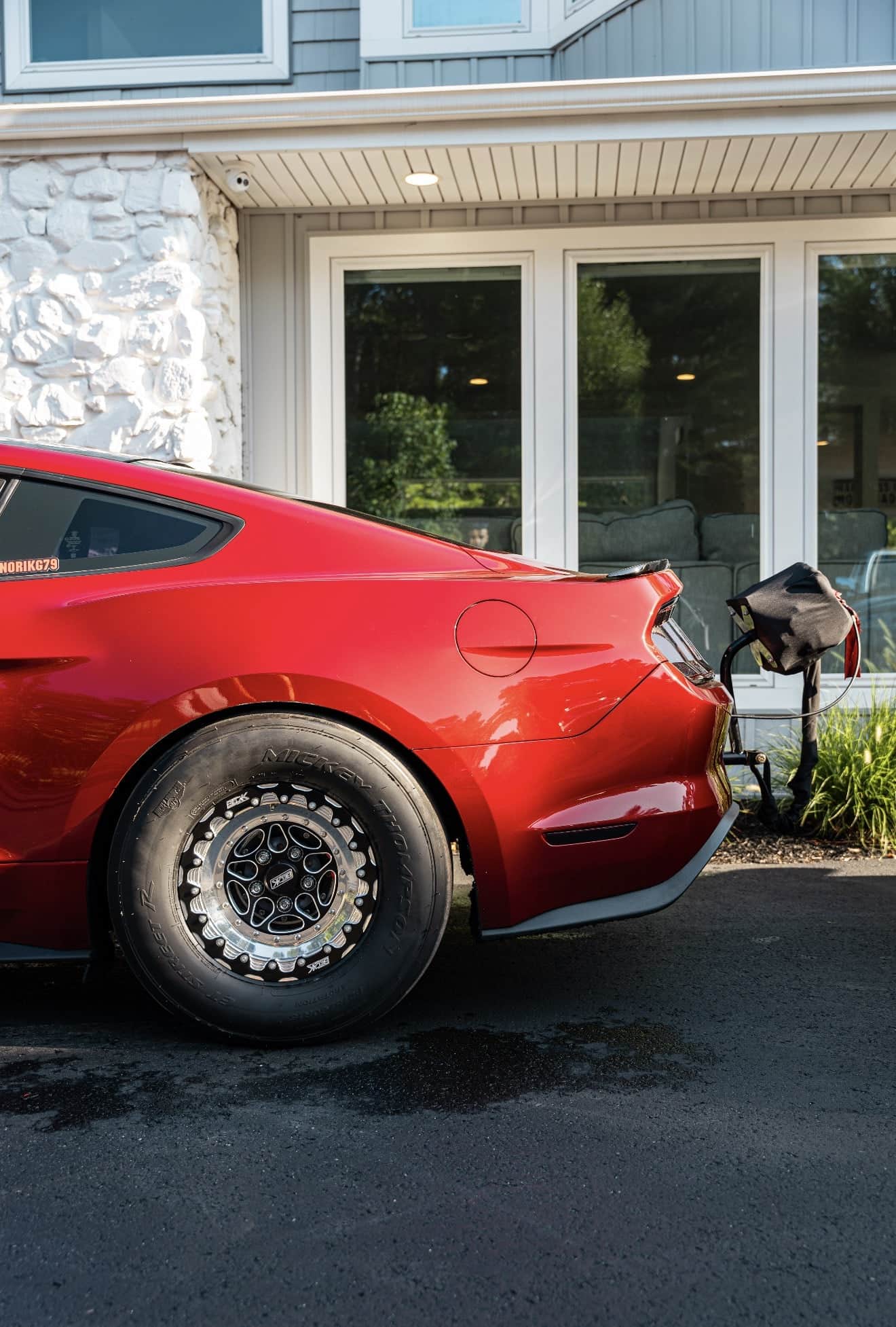 Rear quarter of a red Mustang on a beadlock drag wheel and drag radial, with the parachute mounted behind the bumper