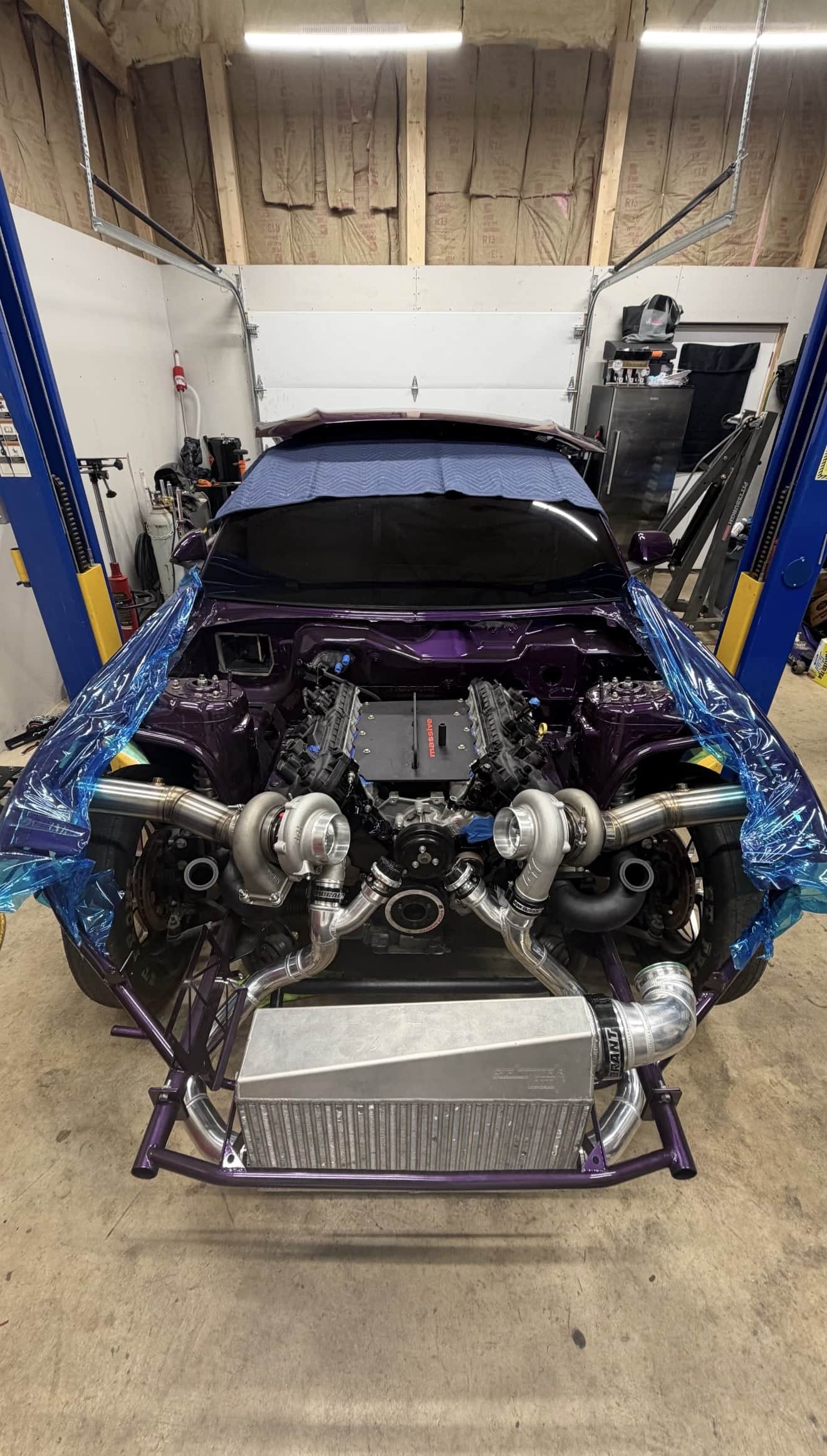 A twin-turbocharged purple car up on the lift at Noro Performance, front end stripped with both turbochargers and the intercooler piping mounted