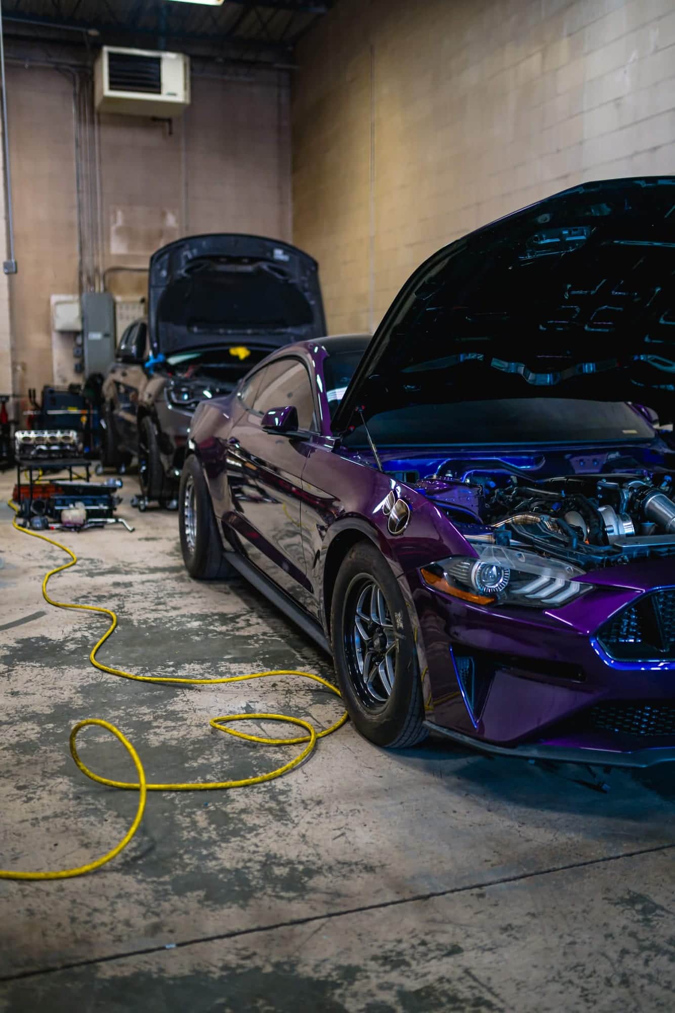 A purple Mustang on drag wheels inside the Noro Performance shop with the hood raised