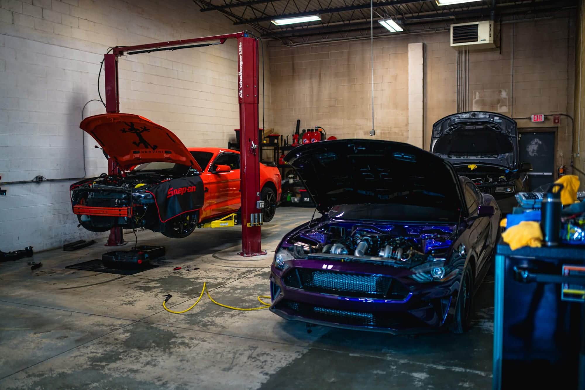 Wide view of the Noro Performance shop with a red Mustang up on the two-post lift and a purple Mustang in front of it