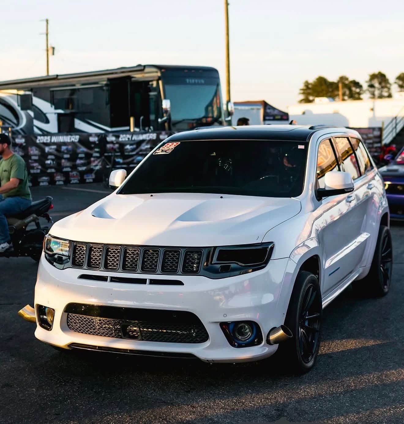 A white Jeep Grand Cherokee Trackhawk parked at an event at sunset