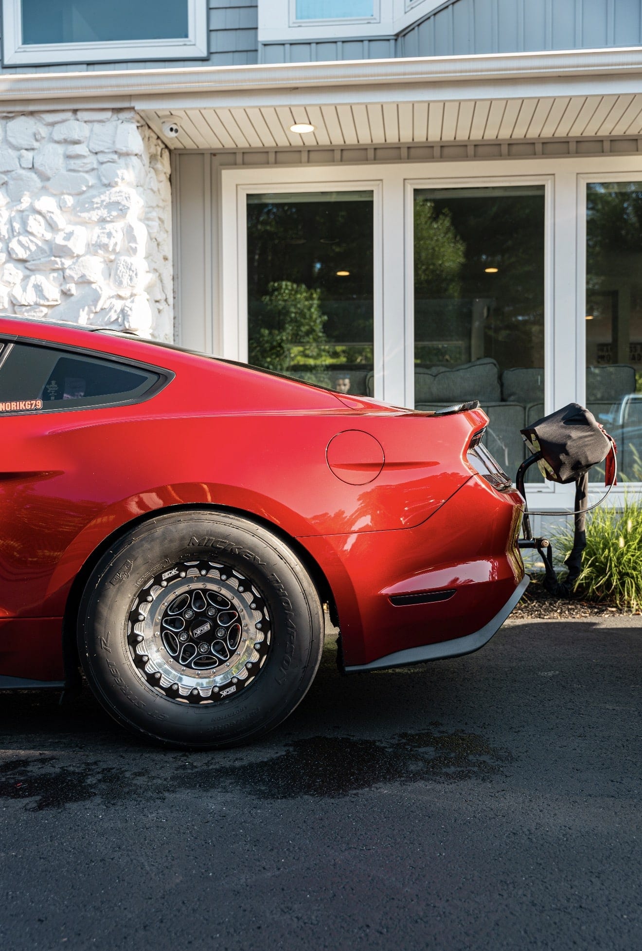 Rear quarter of a red Mustang on a beadlock drag wheel and drag radial, with the parachute mounted behind the bumper