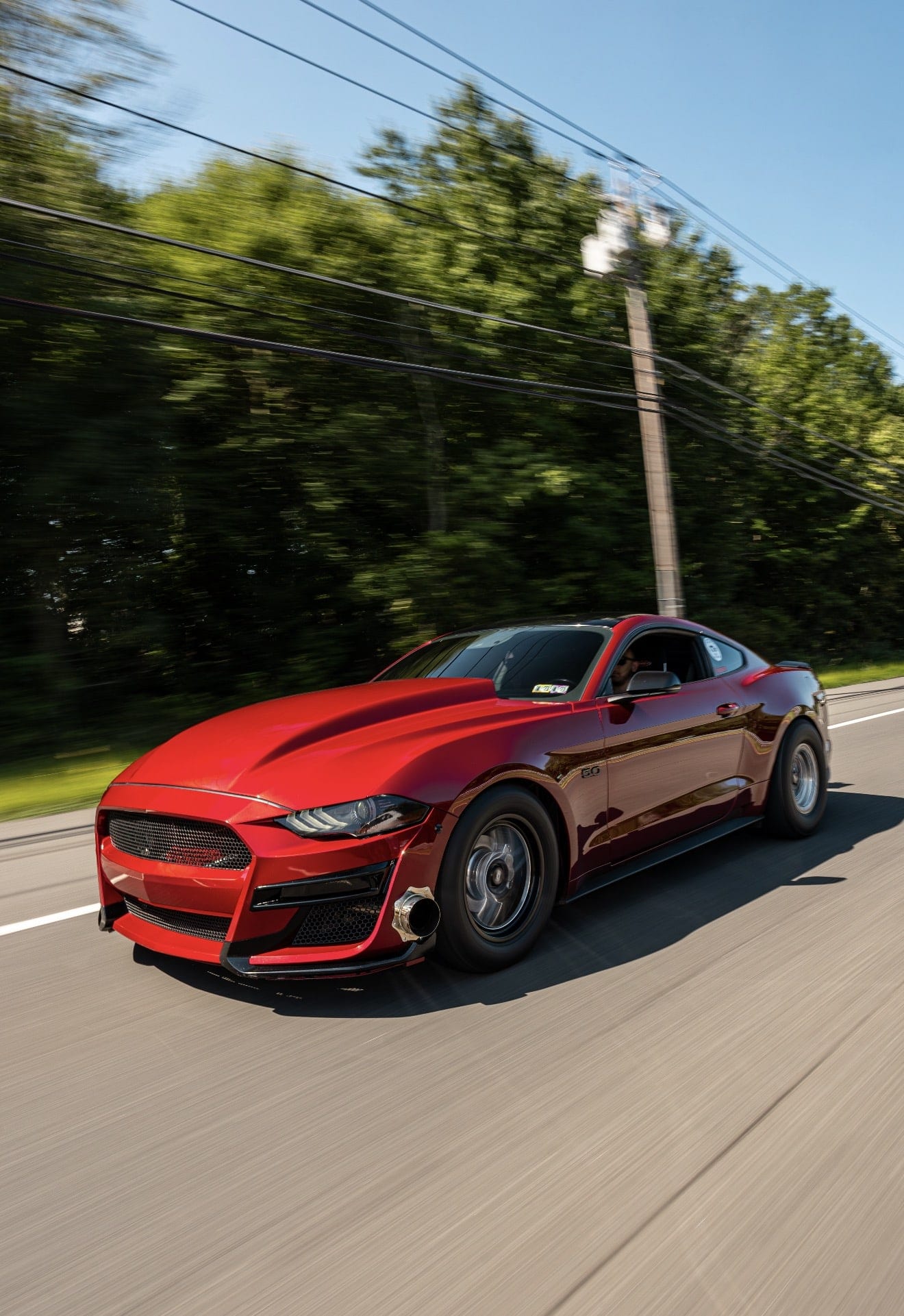A red turbocharged Mustang on drag radials photographed rolling on a country road
