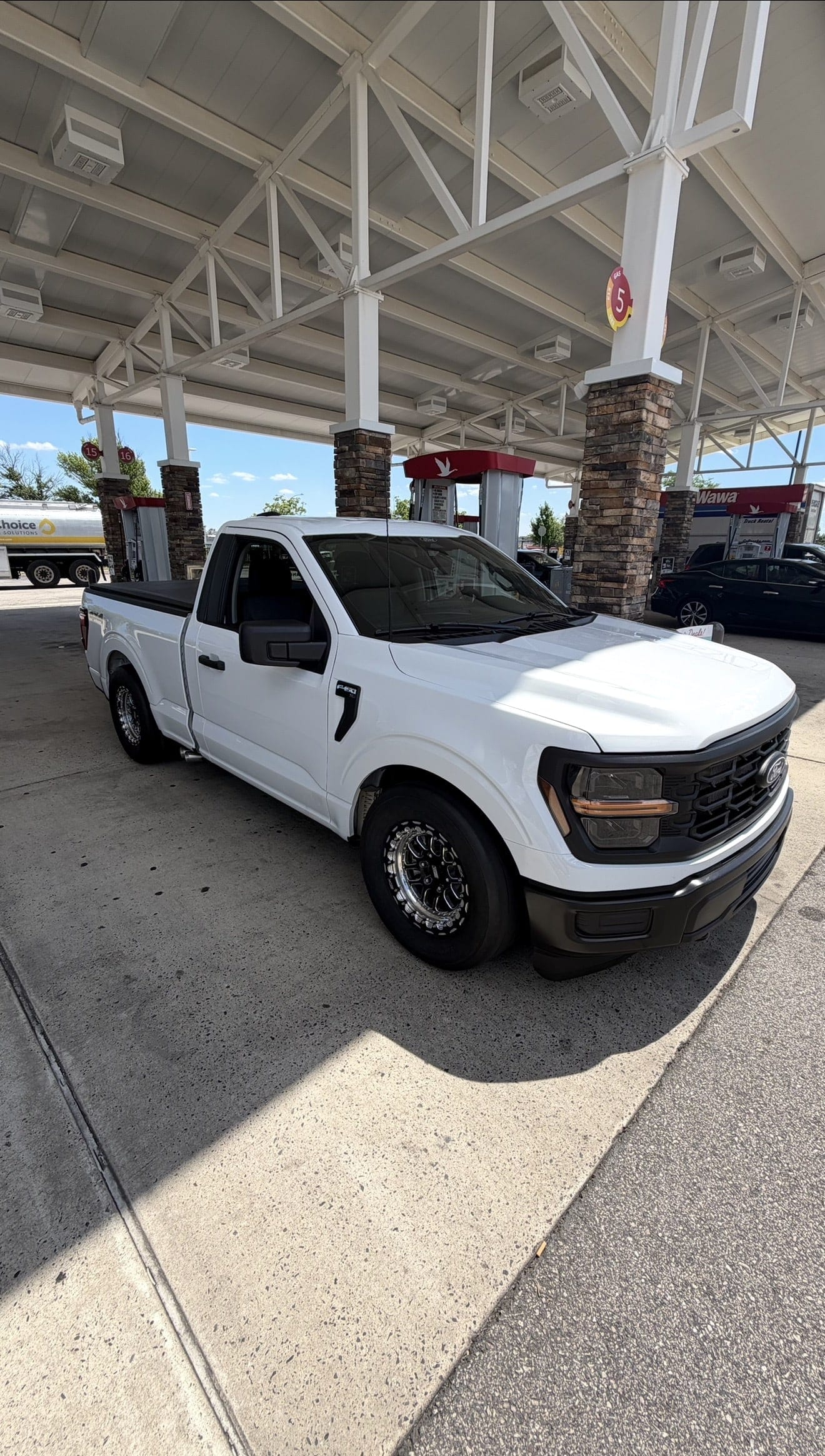A white Ford F-150 regular cab on drag wheels parked at a fuel station