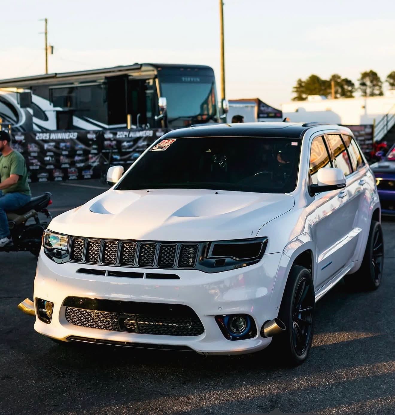 A white Jeep Grand Cherokee Trackhawk parked at an event at sunset