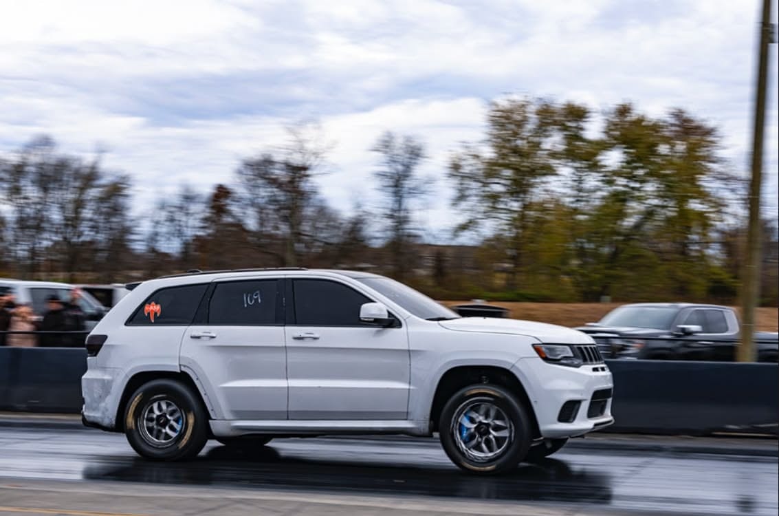 A white Jeep Grand Cherokee Trackhawk on drag wheels making a pass down a drag strip