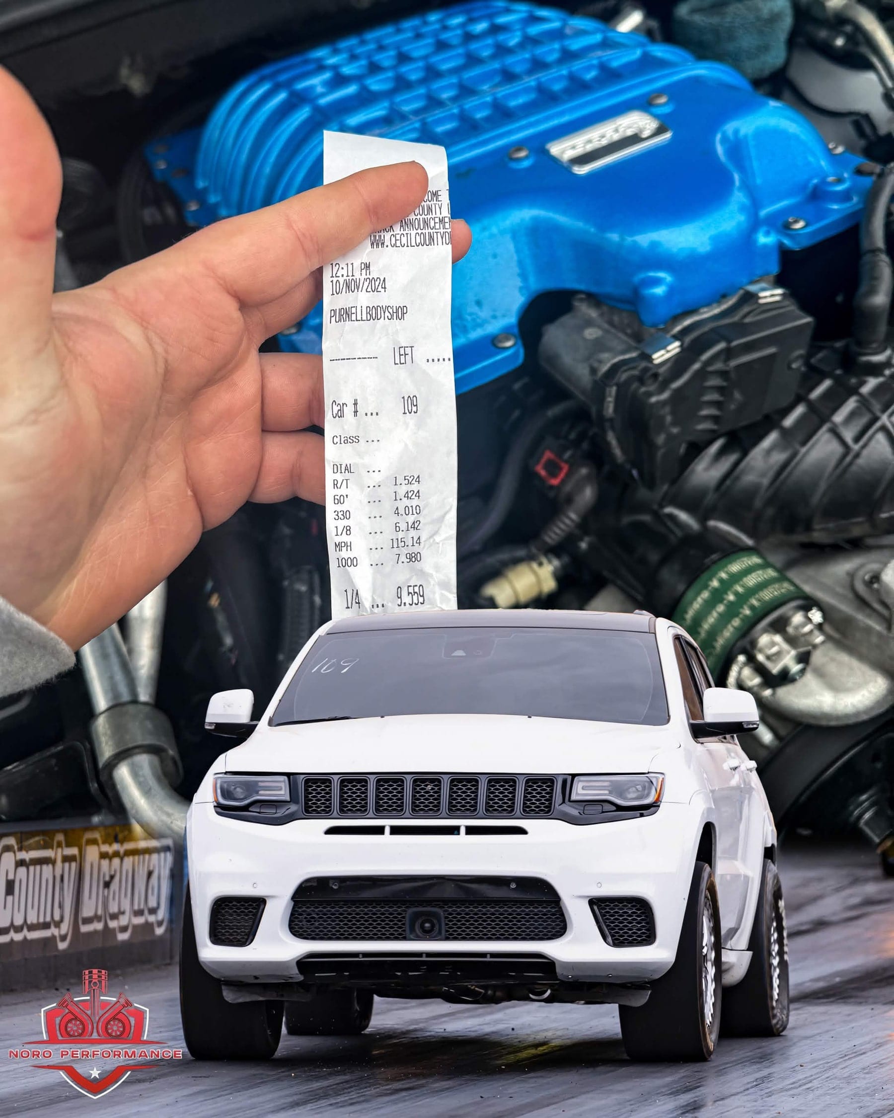 A drag strip time slip held in front of a supercharged engine bay, alongside a white Jeep Trackhawk