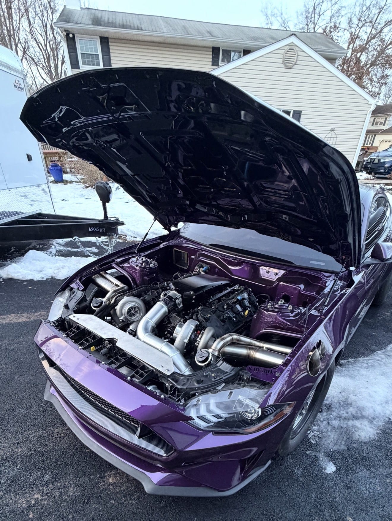 A purple Ford Mustang with the hood raised outside the shop, showing its twin-turbocharged engine